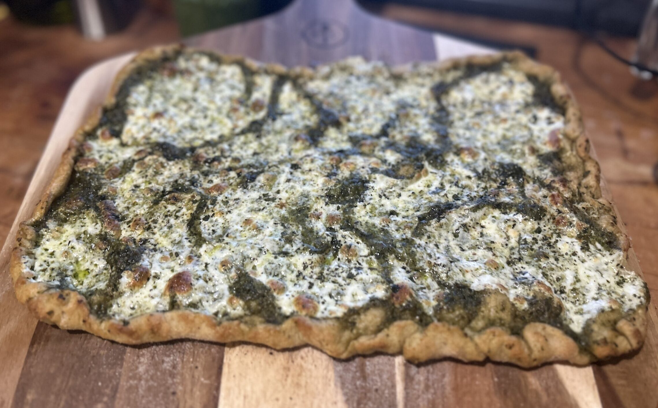 Neopolitan fresh milled pizza with pesto sauce and fresh mozzarella on a wooden pizza peel.